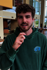 Young man in a green hoodie indoors, holding a small object.