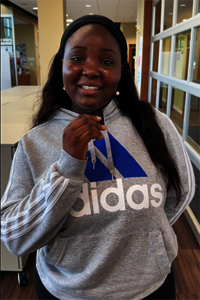 Smiling woman in a gray hoodie stands indoors.