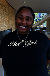 Female student wearing a black "But God" t-shirt indoors.