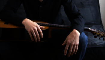 UIS faculty member Adam Larison sitting and holding a guitar