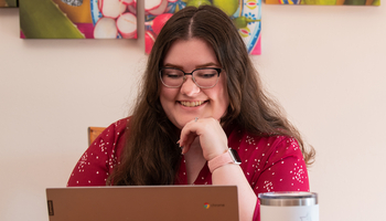 Smiling person using a laptop, colorful artwork in background.