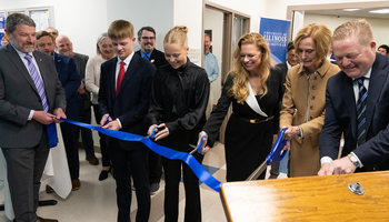 A group of people cutting a blue ribbon at an indoor event.