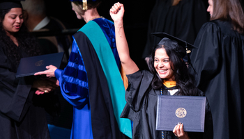 Graduate proudly holding diploma, smiling, surrounded by people in academic gowns.