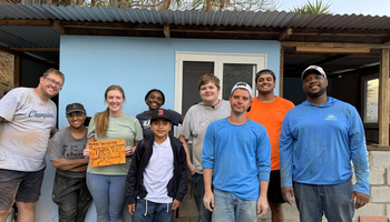 A group of people smiling in front of a light blue house.