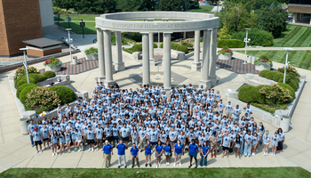 Large group of people in blue shirts gathered outside near circular stone structure.