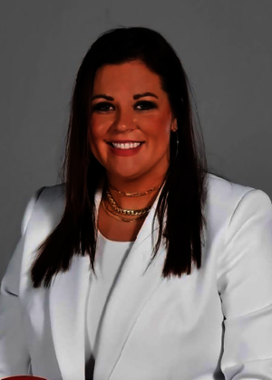 Summer Quesenberry portrait in a white blazer and white top, gold necklaces, long dark hair.