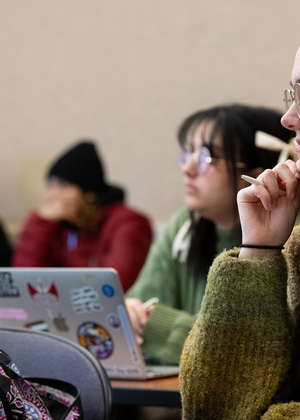 A student in class smiling with a notebook on the desk and pen in hand.