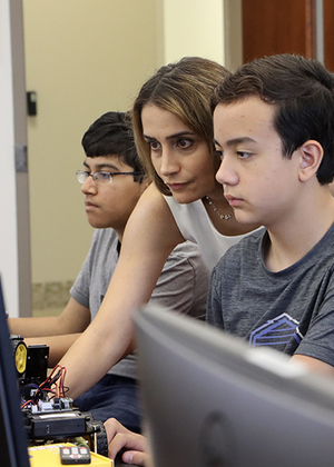 Elham Buxton (center) is shown reaching past a student to control a computer during an AI summer camp.