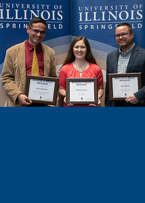 Three faculty members stand holding awards.