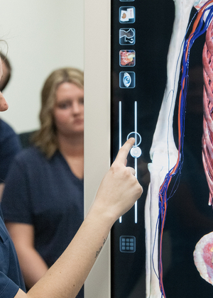 A student stands next to an antomage table, adjusting its functions on the screen.