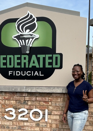 UIS student Wonder Odutola stands next to Federated Fiducial sign.