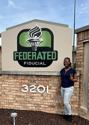 UIS student Wonder Odutola stands next to Federated Fiducial sign.