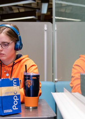 A student wearing headphones uses a laptop computer to study in Brookens Library.