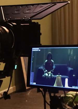 A camera and screen and shown capturing an image of a girl sitting on a couch.