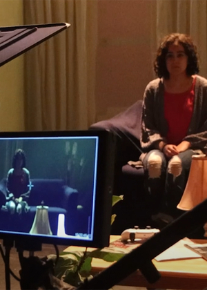 A camera and screen and shown capturing an image of a girl sitting on a couch.