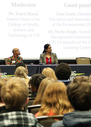 Panelists speak to a large audience at a UIS AI-themed event with a presentation screen in the background.