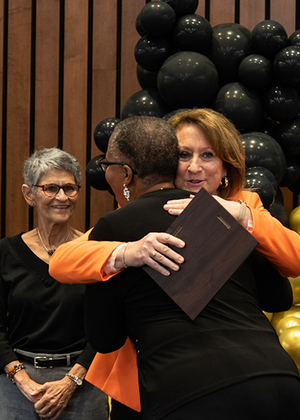 A person receives an award and a hug during the Good as Gold Volunteer Awards ceremony, with others smiling nearby.