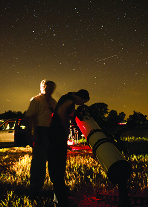 Two people using a telescope to stargaze in a field at night under a star-filled sky.