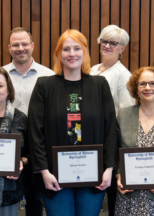 Ten faculty members pose for a photo holding their awards. 