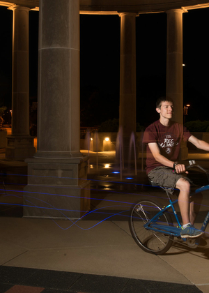 a male student riding his bike through the colonnade at night