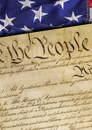 Close-up of the United States Constitution with the words “We the People” visible, placed over an American flag background.
