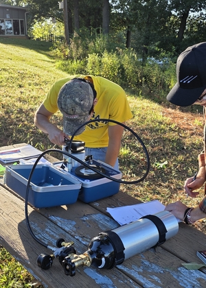 Field scientists operating water quality sensors and documenting plant samples on picnic table at research site