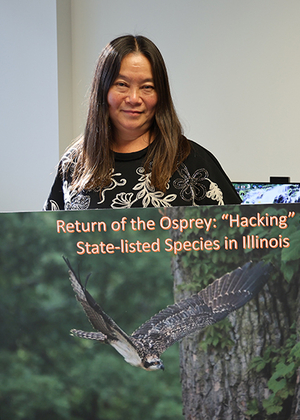 A woman standing, holding a large poster of an osprey in flight.