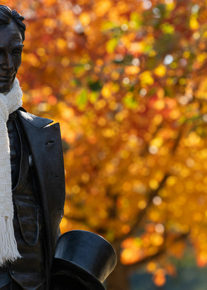 the lincoln statue on the quad has a real scarf wrapped around his neck and there are autumnal leaves on a tree in the background