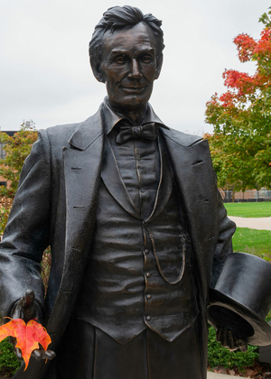 the lincoln statue on campus holding an orange autumn leaf in his hand