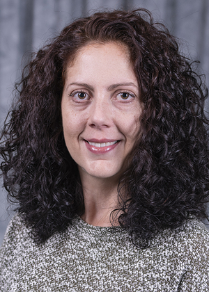 Smiling woman with curly hair against a gray backdrop.