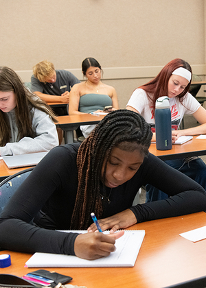Students focused on writing at desks in a classroom.