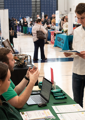 Man in white shirt talks to seated people at a busy job fair.