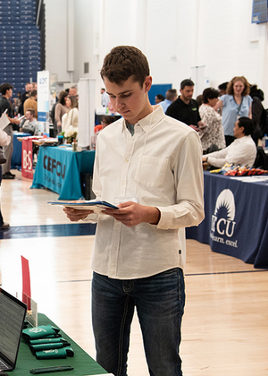 Young man reading a brochure at a busy indoor event with booths.