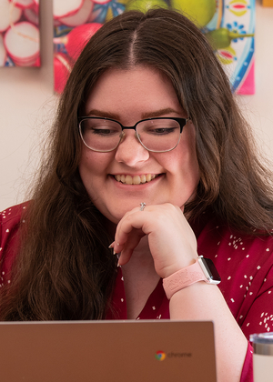 Smiling person using a laptop, colorful artwork in background.