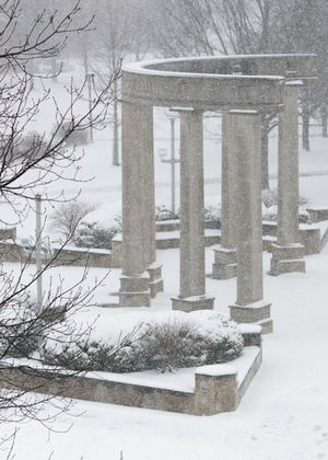 Snow-covered colonnade and trees in a wintry scene.