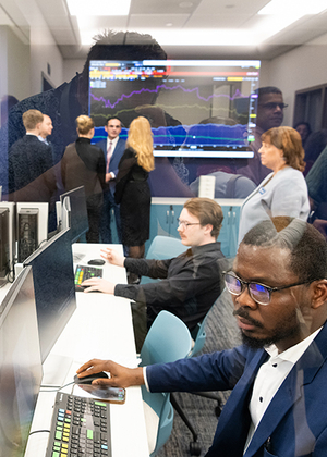 People working at computers in an office with a stock market screen.