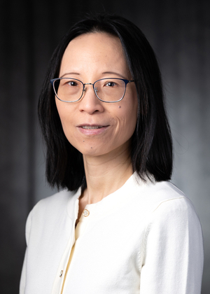 Woman with glasses, wearing a white top against a dark backdrop.