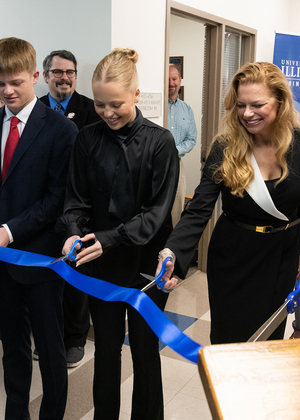 A group of people cutting a blue ribbon at an indoor event.