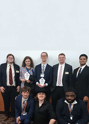 Eight people in formal attire, two holding awards, smiling indoors.