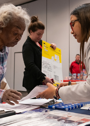 Two women exchanging documents at a crowded conference table.