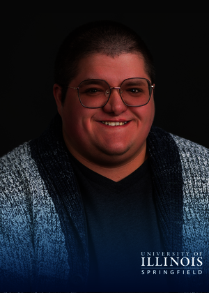Smiling person wearing glasses and a textured cardigan, dark background.