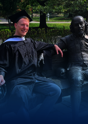 Graduate sitting next to a statue on a bench in a park setting, smiling.