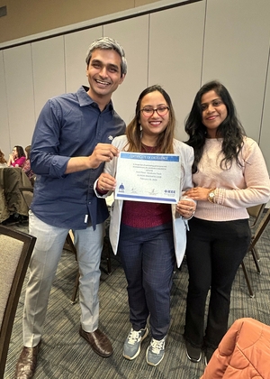 Three people smiling, one holding a certificate in a conference room.