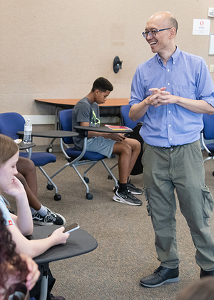 Man in blue shirt speaking to students in a classroom setting.