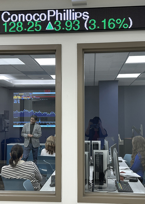 Office meeting seen through a window, stock ticker overhead.