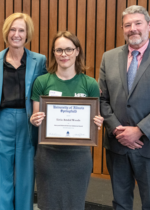 Three people standing, one holding a framed certificate.