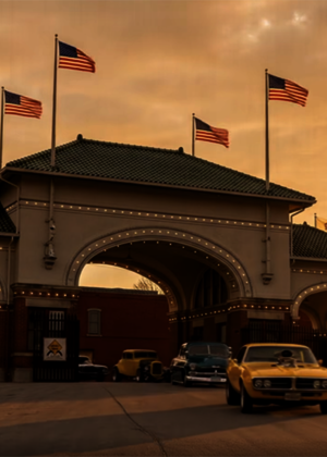 Historic gateway at sunset, vintage cars parked, flags waving.