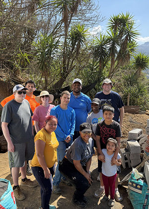 Group of people posing outdoors with trees and mountains in the background.