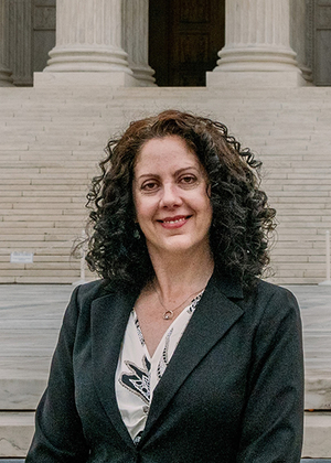 Woman in a suit smiling in front of a building with large steps.