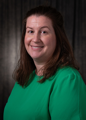 Smiling woman in a green shirt against a dark background.
